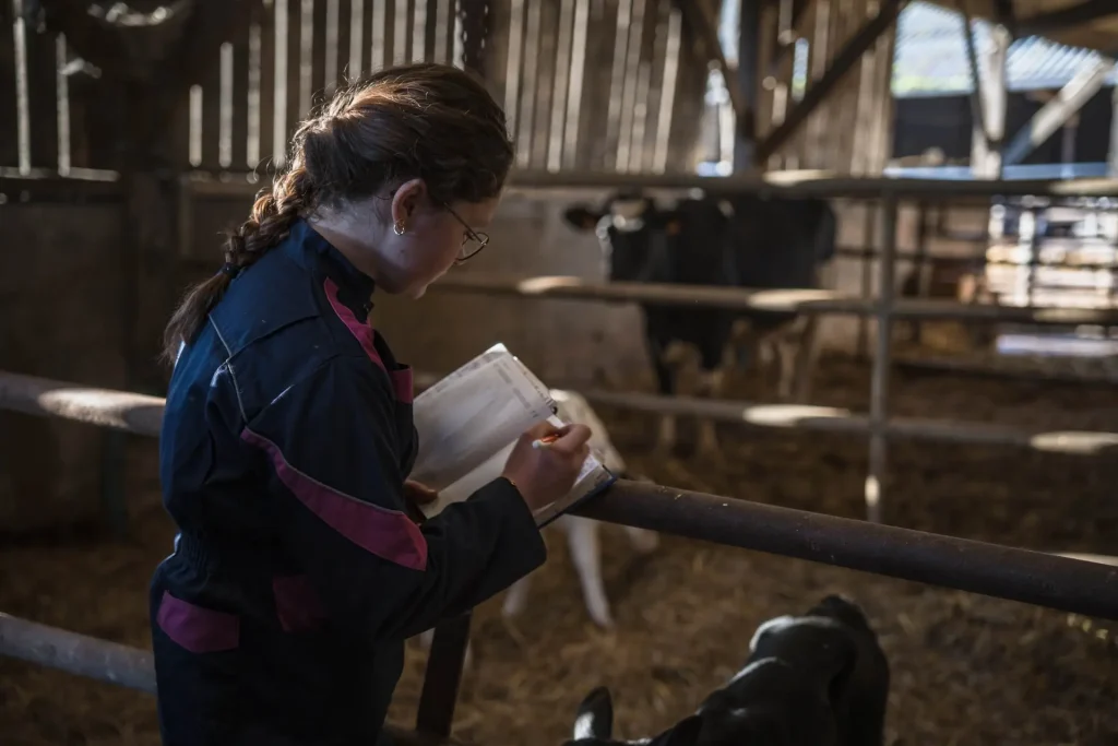 Élève de 1re Bac Pro CGEA qui note les soins dans le carnet sanitaire, accoudée à la barrière de la stabulation